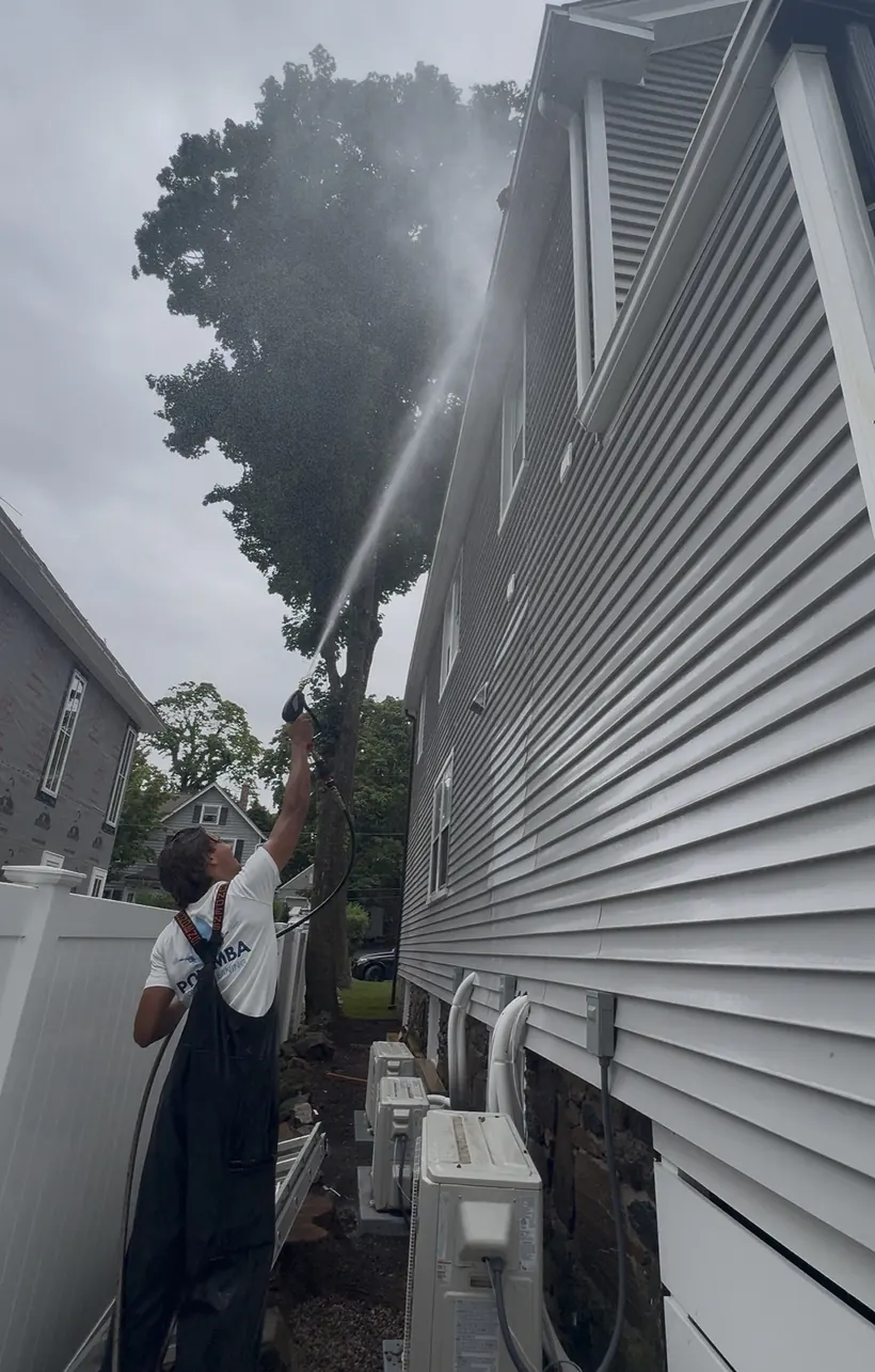A Povemba brother soft washing the side of a gray two-story house