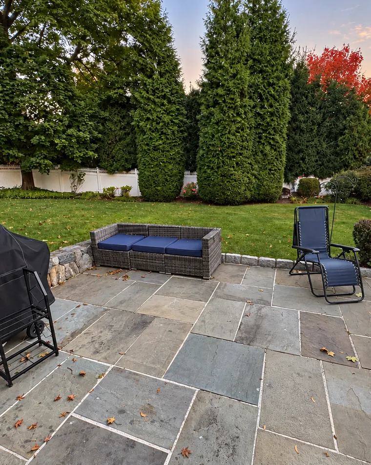 A wicker patio sofa with blue cushions on a bluestone patio in the fall